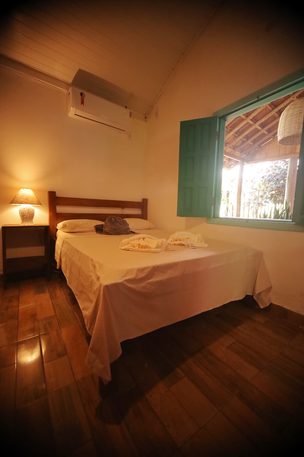 Cama de casal da Suíte Standard com janela verde e ar-condicionado